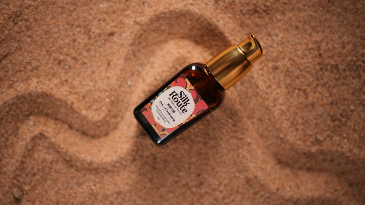 A bottle of Dew of Dunhuang Hydrating Serum placed on a textured sandy background.