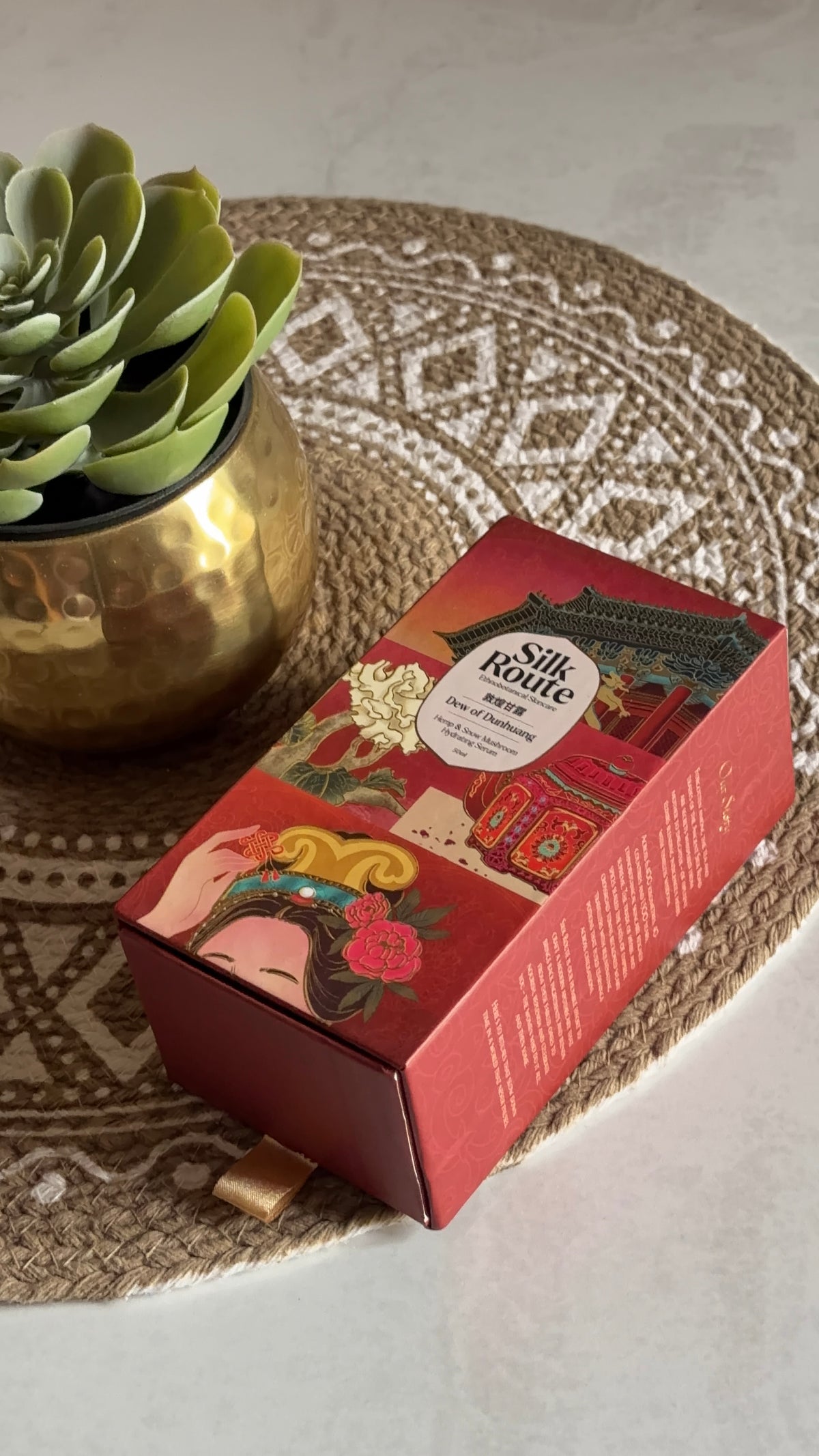 Silk Route Dew of Dunhuang Serum bottle styled in warm natural light on a table
